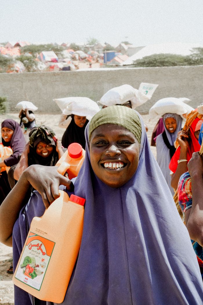 A smiling woman carries aid supplies in a community setting, Africa.