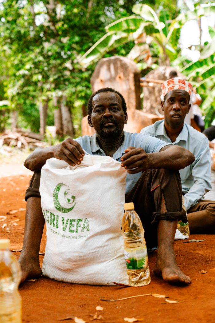 Two men sitting outdoors with food supplies, showcasing aid distribution.